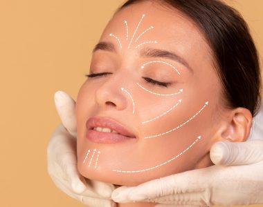 Beauty treatment concept. Young woman receiving face massage from cosmetologist, doctor wearing protective gloves, beige studio background, cropped